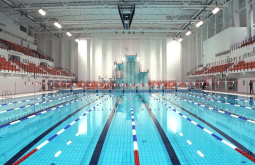 Tory, 50 m basenu wypełnionego wodą. Po bokach trybuny z pomarańczowymi krzesełkami.