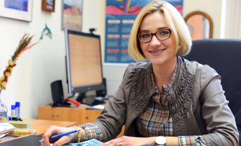 Zdjęcie portretowe: Dr Aleksandra Ziemińska-Stolarska siedzi uśmiechnięta przy biurku w swoim gabinecie. W tle urządzenia biurowe.