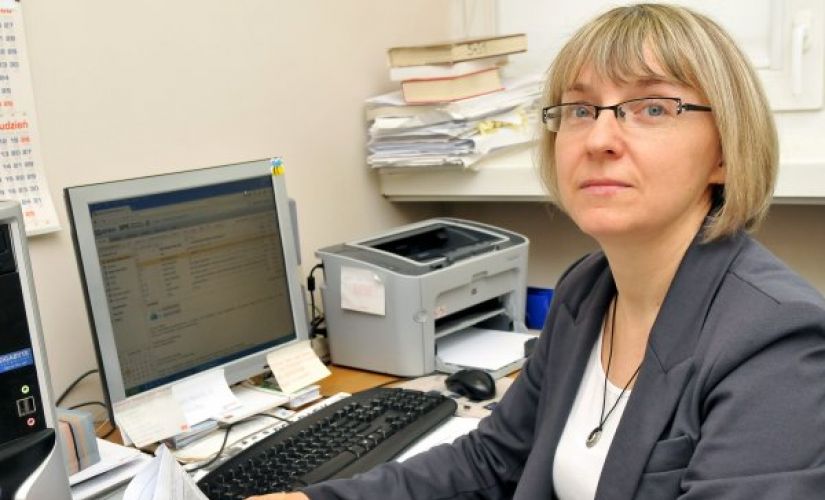 Zdjęcie portretowe: dr inż. Janina Leks-Stępień siedzi przy biurku. W tle dokumenty, komputer i drukarka.