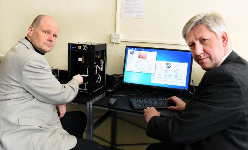 Zdjęcie portretowe: dr hab. Konrad Olejnik i dr inż. Paweł Pełczyński siedzą przy stanowisku komputerowym. 