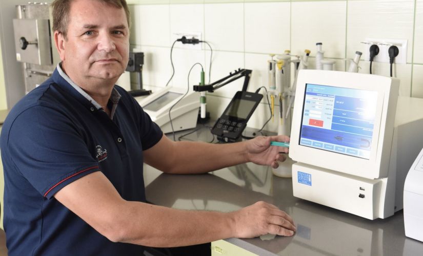 Zdjęcie portretowe: dr hab. inż. Piotr Dziugan w niebieskiej polówce przy stole laboratoryjnym na którym stoi urządzenie pomiarowe. 