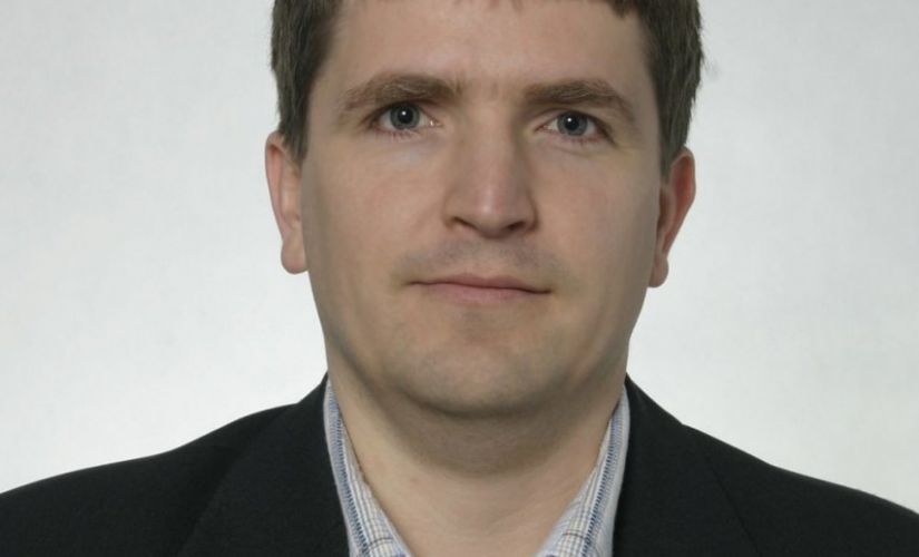 Zdjęcie portretowe: dr inż. Łukasz Frącczak w ciemnej marynarce na białym tle.