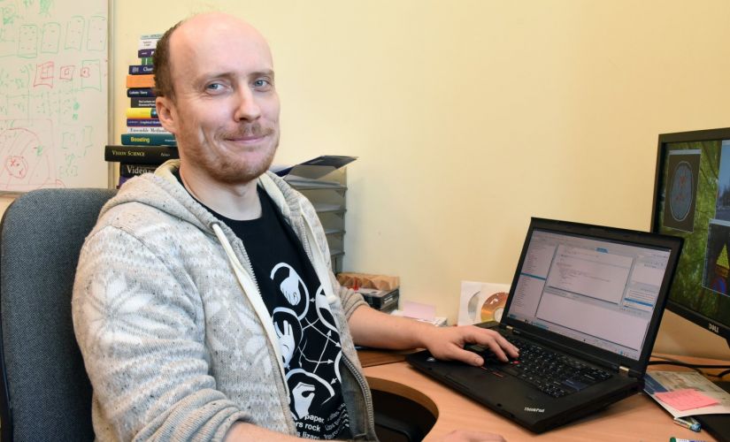 Zdjęcie portretowe: dr inż. Arkadiusz Tomczyk przy biurku, na którym stoi włączony laptop.
