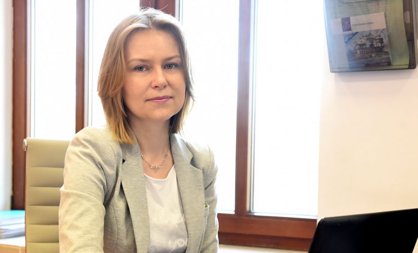 Zdjęcie portretowe: dr inż. Edyta Marcinkiewicz siedzi w gabinecie przy biurku i otwartym laptopie.