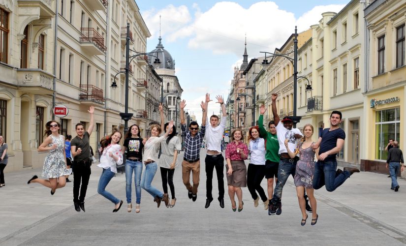 14 zagranicznych studentów uchwyconych w podskoku na ul. Piotrkowskiej w słoneczny dzień.