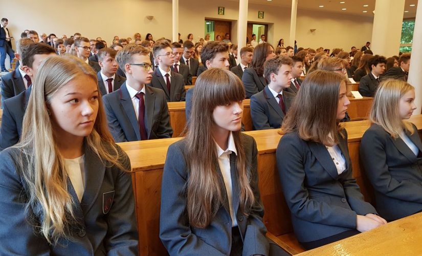 Uczniowie PLO PŁ w szarych, jednolitych marynarkach siedzą w rządach podczas inauguracji roku szkolnego.