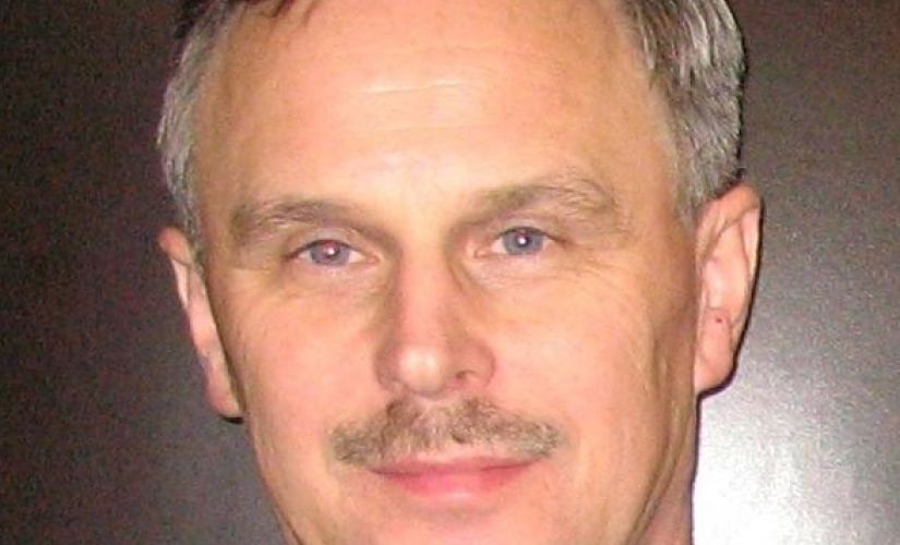 Zdjęcie portretowe: dr inż. Adam Rylski w czarnym garniturze i białej koszuli na szarym tle.