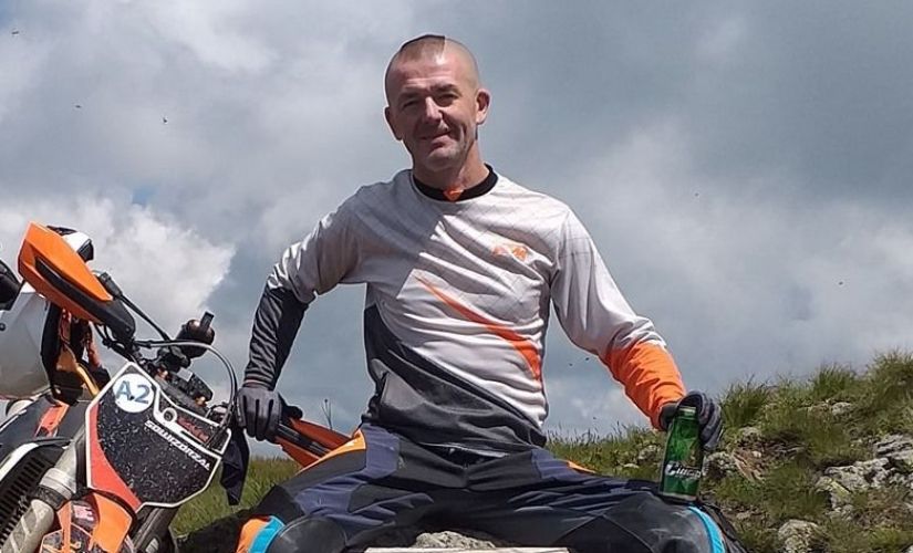Prof. A. Niewiadomski w motocyklowym stroju sportowym siedzi na skale. Obok ubłocony motor.