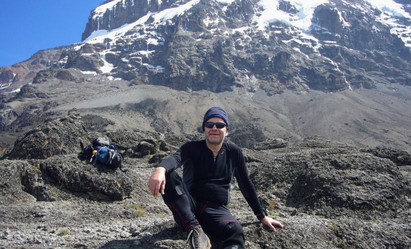 Prof. J. Banasiak ubrany w czarny sportowy strój na tle gór - masywu Uhuru Peak (Kilimandżaro).