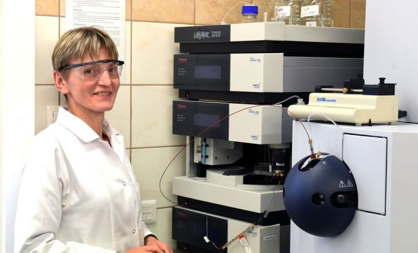 Prof. Beata Kolesińska w białym fartuchu i ochronnych okularach stoi przy stanowisku laboratoryjnym.