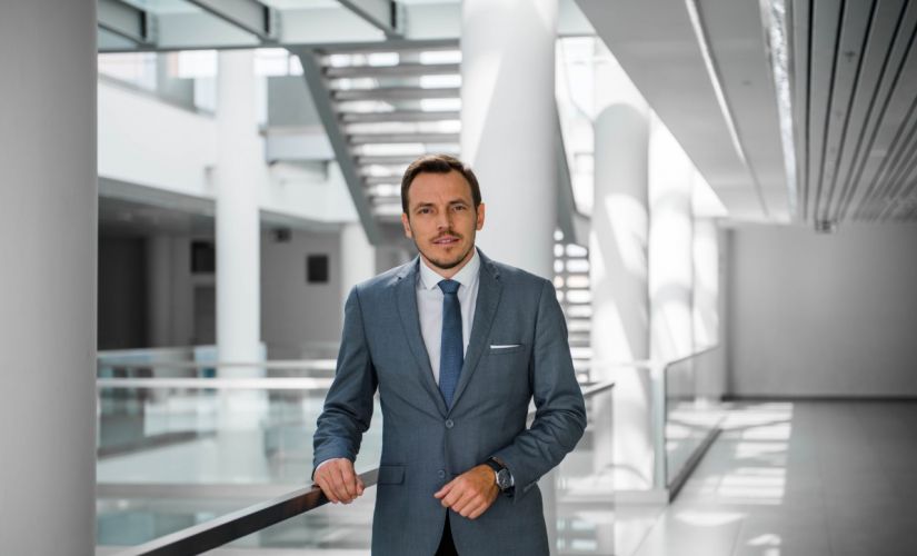 dr Dariusz Koperczak w szarym garniturze stoi na tle przestrzeni w nowoczesnym gmachu