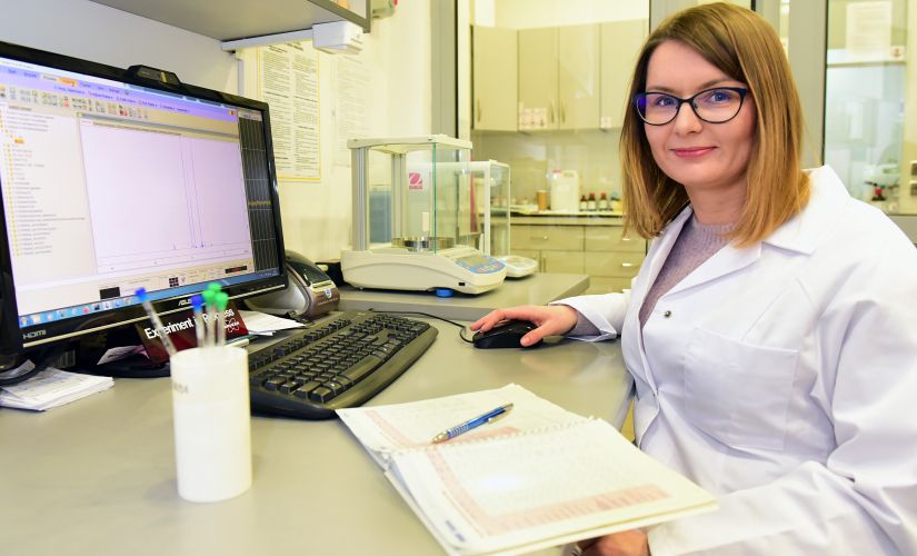 kobieta naukowiec siedzi przed komputerem w laboratirium ubrana w biały fartuch