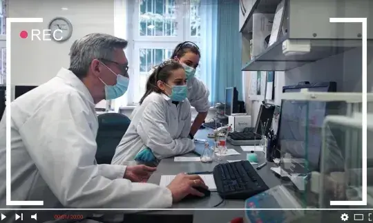 Trzech naukowców w białych fartuchach przy stole laboratoryjnym.