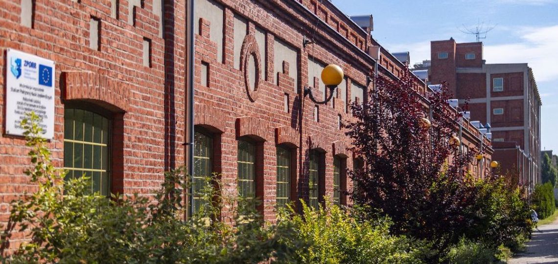 Długi, parterowy budynek z cegły - siedziba Centrum Językowego PŁ. Wzdłuż ściany zielone krzaki.