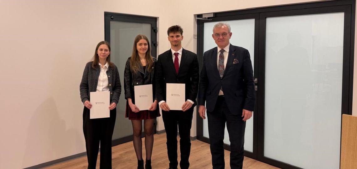 Troje młodych osób z dyplomami w rękach stoi w towarzystwie eleganko ubranego mężczyzny