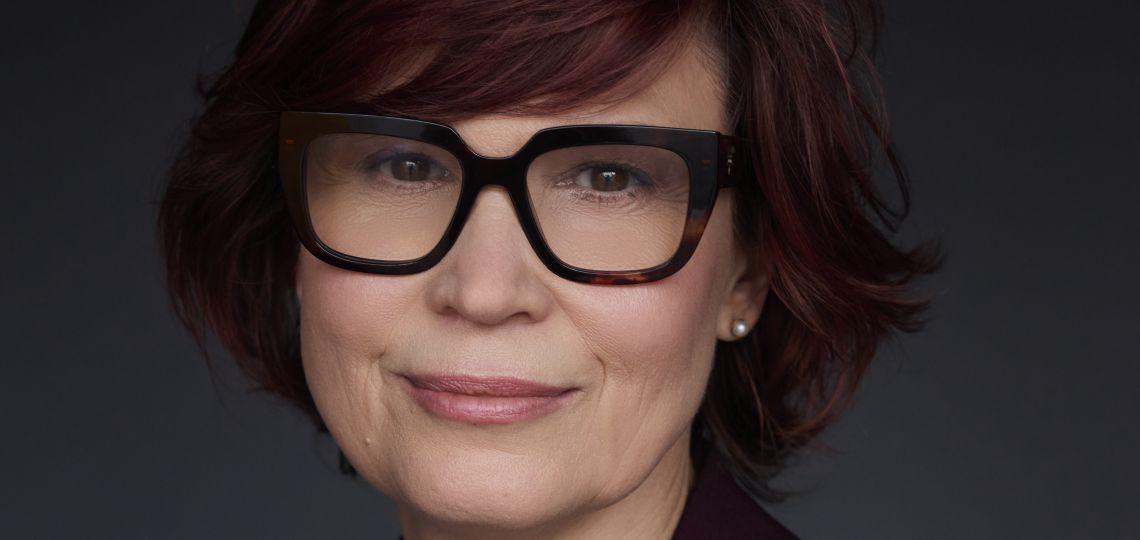 portret uśmiechniętej kobiety w okularach, ciemne tło, ciemna marynarka, błękitna bluzka, prof. Edyta Gendaszewska-Darmach