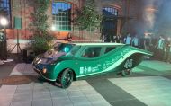 Eagle Two - elektryczny samochód zespołu Lodz Solar Team o nowoczesnym designie w kolorze zielonym na tle ceglanej zabudowy.