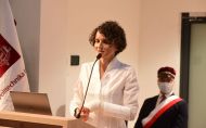 prof. Katarzyna Pernal w białej bluzce stoi przy mównicy podczas wykładu inauguracyjnego.