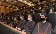 Studenci w togach oraz maskach siedzą na widowni podczas inauguracji roku akademickiego.