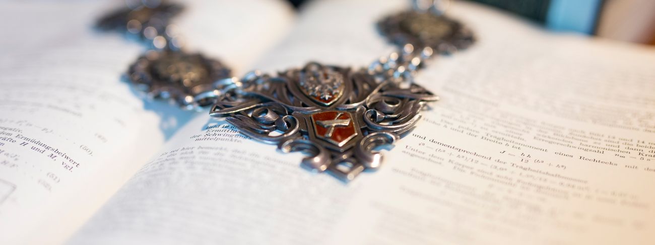 Fragment łańcucha rektorskiego na tle otwartej księgi.