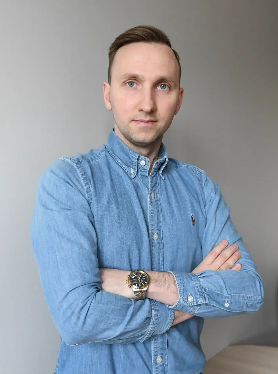 zdjęcie młodego mężczyzny w błękitnej koszuli stojącego na tle beżowej ściany