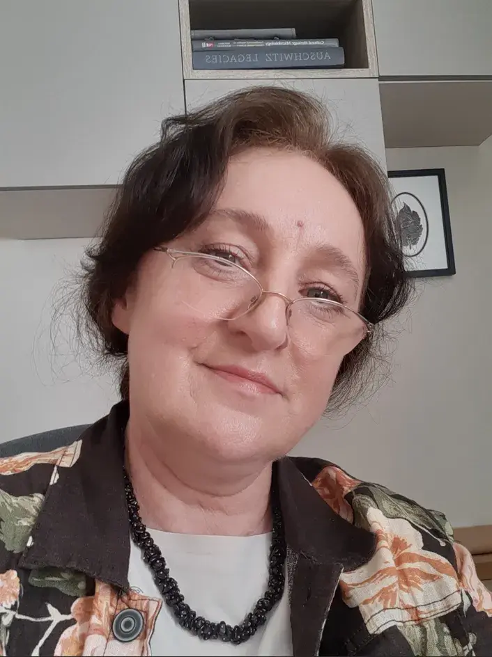 portret kobiety w średnim wieku i okularach opuszczonych na nos, na tle beżowej ściany