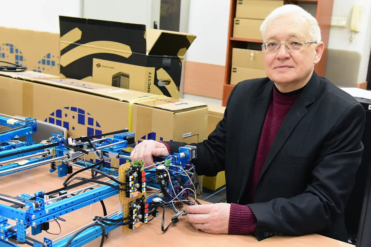 prof. V. Mosorov siedzi w ciemnym stroju, okularach, przy biurki z prototypem urządzenia