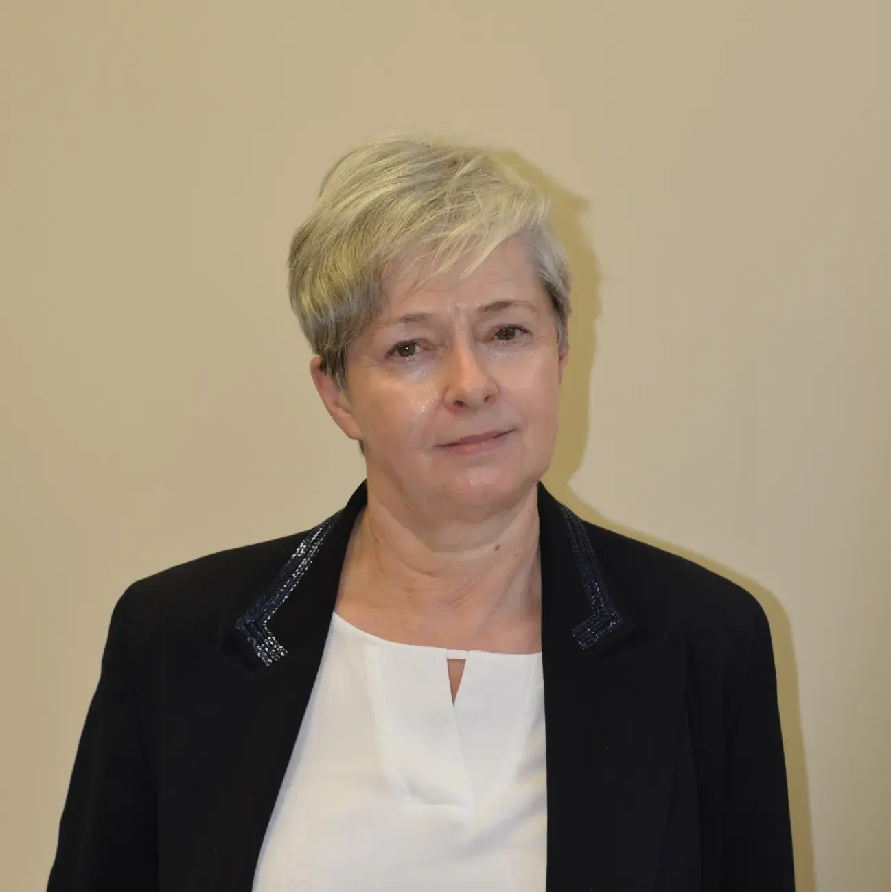 portret kobiety z krótkimi blond włosami, w czarnej marynarce, białej bluzce, w tle żółta ściana, prof. Maria Koziołkiewicz