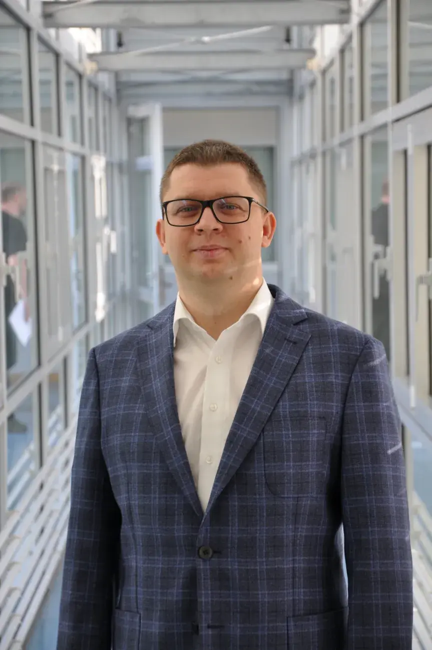 męczyzna w okularach, marynarce i białej koszuli stoi w wąkim jasnym korytarzu, Tomasz Marszałek
