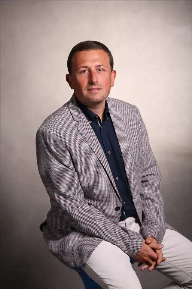 siedzący w marynarce, na szarym tle, Radosław Wajman