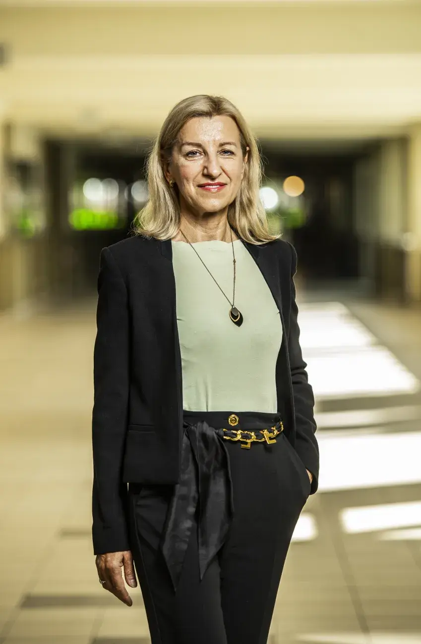 kobieta w blond włosach uśmiecha się, stoi w korytarzu, ubrana elegancko, ciepła kolorystyka, prof. Grażyna Budryn