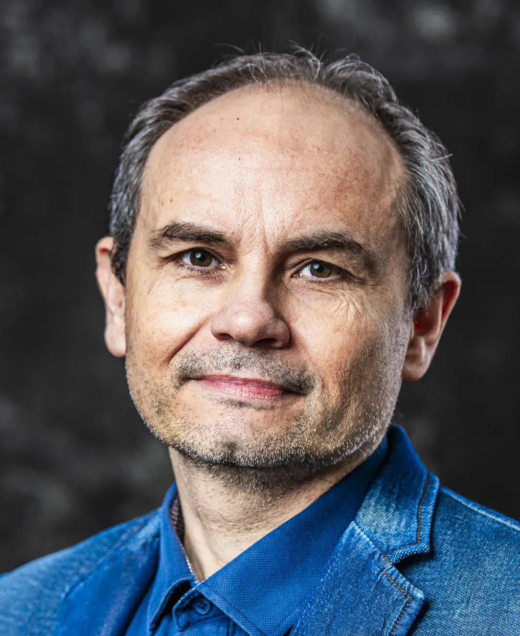 portret mężczyzny w granatowej marynarce, patrzy wprost, lekko siwe włosy