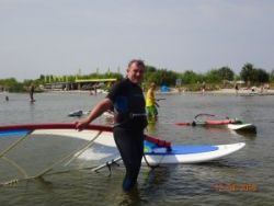Prof. Krzysztof Jóźwik w sportowym stroju stoi w jeziorze i trzyma deskę surfingową z żaglem.