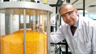 Portrait photo: Prof. Andrzej Górak, wearing a white lab coat and safety goggles, stands next to a transparent container filled with yellow granules.