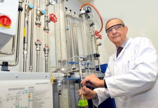 Portrait photo: Prof. Andrzej Górak, wearing a white lab coat and safety goggles, stands next to a specialised device.
