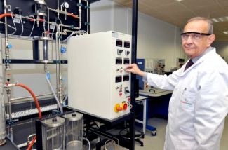 Portrait photo: Prof. Andrzej Górak, wearing a white lab coat and safety goggles, stands next to a specialised device.