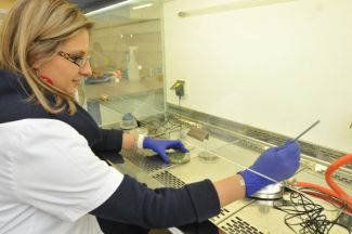 Zdjęcie portretowe: członkini zespołu prof. Beaty Gutarowskiej w białym fartuchu i rękawiczkach dokonuje badań laboratoryjnych.