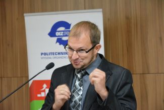 dr hab. inż. Grzegorz Szymański stoi przy mównicy i udaje, że boksuje.