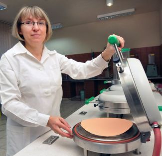 Portrait photo: Dr Eng. Janina Leks-Stępień in a white coat in left profile is sitting at a specialist apparatus.