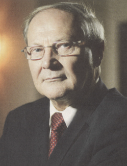 Zdjęcie portretowe wykadrowane: prof. Władysław Mielczarski w ciemnej marynarce, białej koszuli i czerwonym krawacie.