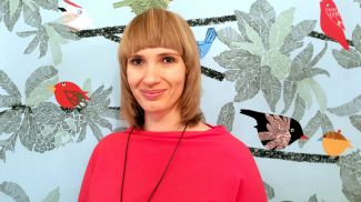 Zdjęcie portretowa: uśmiechnięta dr hab. Małgorzata Koszewska w czerwonej bluzce na tle abstrakcyjnej grafiki.