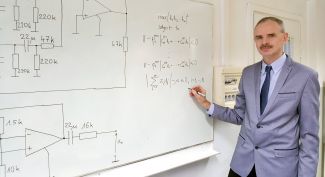 Portrait photo: Assoc. Prof. Stanisław Hałgas, TUL Prof. wearing a suit, is standing by a white board with technical drawings on it.