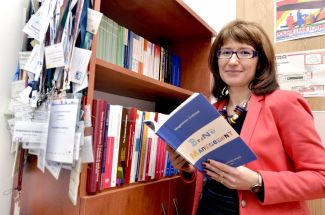 Portrait photo: Assoc. Prof. Eng. Magdalena Grębosz-Krawczyk, TUL Prof. is standing by a bookcase. She is holding one of the books open in her hands.