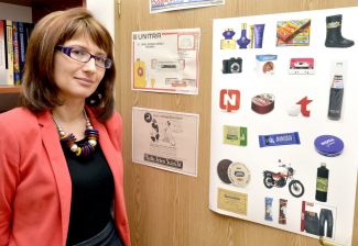 Portrait photo: smiling Assoc. Prof. Eng. Magdalena Grębosz-Krawczyk, TUL Prof. wearing a red jacket, is standing next to a cork board with colourful pictures.