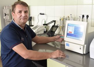 Zdjęcie portretowe: dr hab. inż. Piotr Dziugan w niebieskiej polówce przy stole laboratoryjnym na którym stoi urządzenie pomiarowe. 