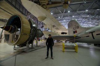 Zdjęcie portretowe: dr inż. Grzegorz Liśkiewicz w hangarze. W tle dominujące konstrukcie samolotów.