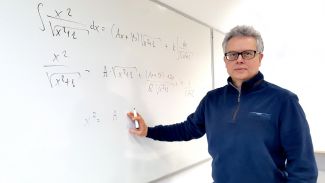 Zdjęcie portretowe: dr inż. Jakub Szczepaniak stroi przy białej tablicy z czarnymi, matematycznymi  wzorami.