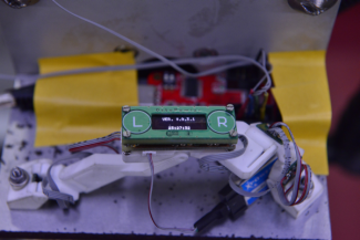 Laboratory instrument. In the foreground a green meter with L and R buttons and display. In the background different coloured elements: yellow, red, purple and connecting wires.