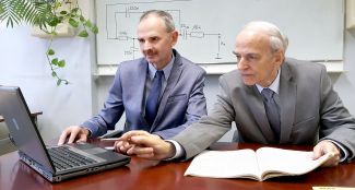Portrait photo: Prof. Dr. Michał Tadeusiewicz Assoc. Prof. Eng. and Assoc. Prof. Eng. Stanisław Hałgas, TUL Prof. in their suits sitting at their desks and working on the laptop.