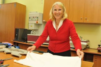 Uśmiechnięta prof. Izabella Krucińska w czerwonym swetrze w laboratorium prezentuje biały materiał z którego wykonywane są biodegradowalne maseczki.
